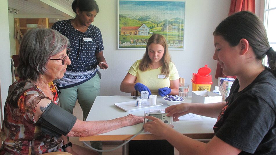 Angeleitet von Pflegedienstleiterin Nila Ekubo messen die beiden Fachfrau-Gesundheit-Lernenden Siri Klee (rechts) und Salome Eugster den Blutdruck einer Besucherin. (Bild: Peter Eggenberger)